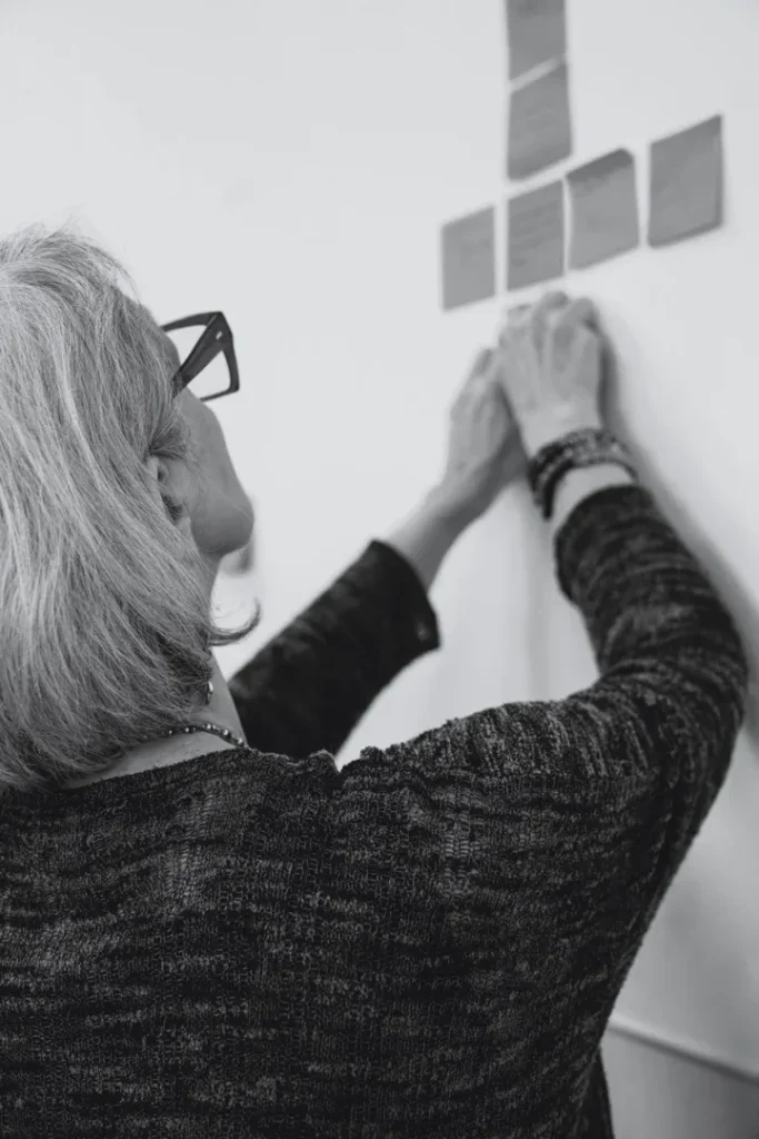 A woman reaching up to place or adjust sticky notes on a wall.
