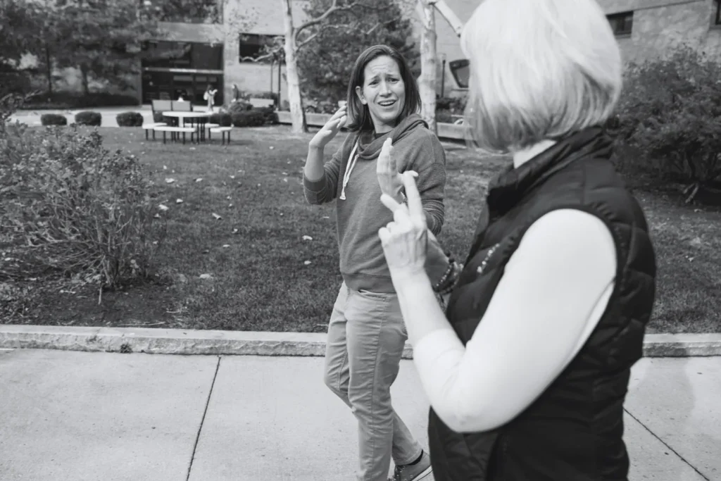 Two individuals gesturing during a conversation, with the focus on a woman in a hoodie expressing herself vividly.
