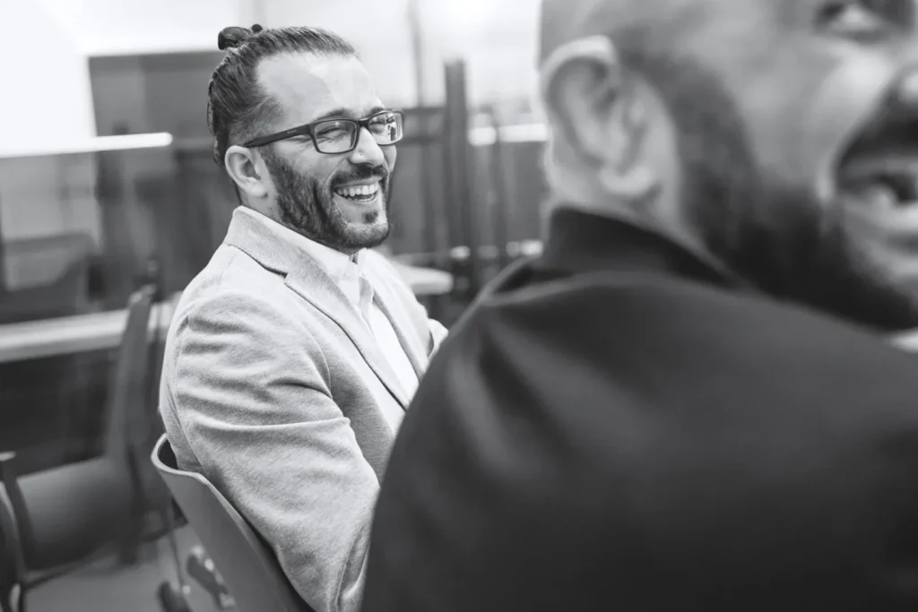A man with glasses and a bun hairstyle laughing and looking to his side.