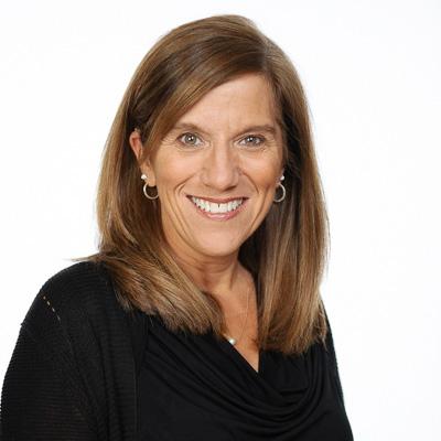 A smiling woman, Karen Hopkins with shoulder-length light brown hair wearing a black outfit against a plain white background.