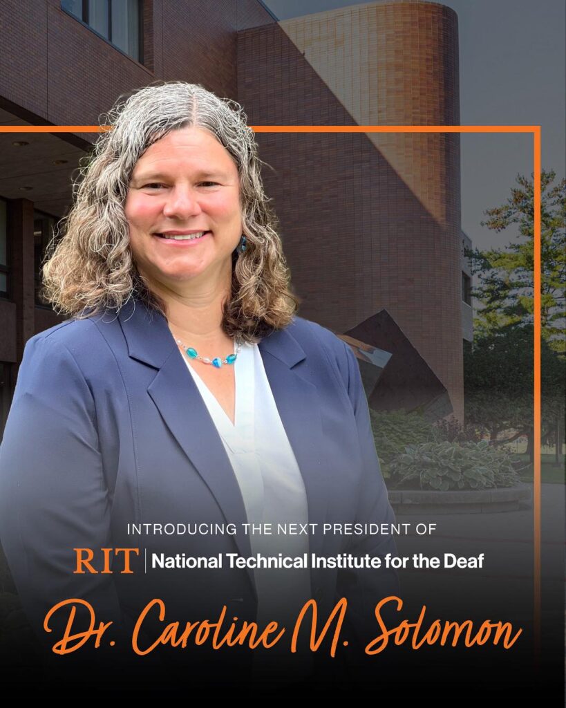A professional portrait of Dr. Caroline M. Solomon, who is smiling and wearing a dark blue blazer over a white top, with a turquoise necklace and curly gray-and-brown shoulder-length hair. She stands in front of a modern brick academic building with curved and angular architecture. The background is subtly darkened, with an orange rectangular frame highlighting the subject. Text on the image reads: “Introducing the next president of RIT | National Technical Institute for the Deaf. Dr. Caroline M. Solomon.”