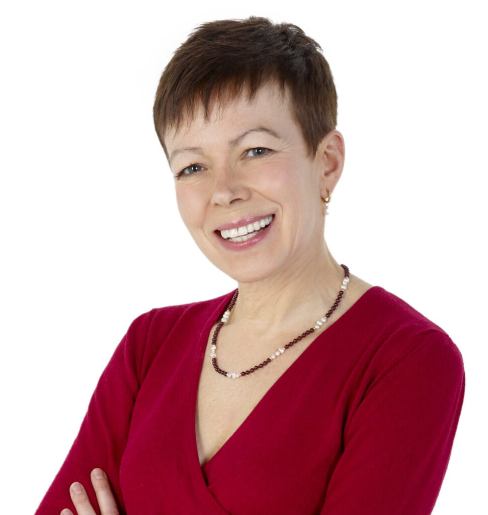 A smiling woman, Dr. Debra Russel stands with her arms crossed, wearing a red long-sleeve top and gray pants against a white background.