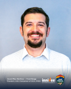 Smiling headshot of a person with short dark hair and a mustache/goatee, wearing a light sweater over a collared shirt against a light blue-gray background. Bottom text shows name and titles; inniVee Strategies and Deaf TRAIL logos at bottom right.